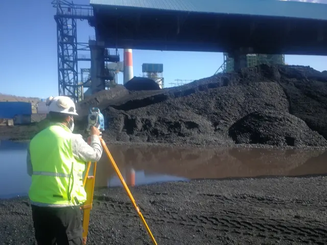 Topógrafo con estación total frente a un acopio de carbón